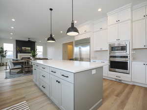 Kitchen featuring white cabinets, ceiling fan, light hardwood / wood-style floors, hanging light fixtures, and built in appliances