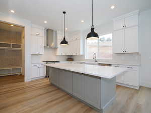 Kitchen with wall chimney range hood, white cabinetry, a kitchen island, light wood-type flooring, and decorative light fixtures