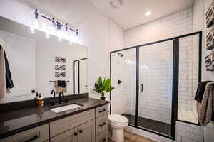 Bathroom with wood-type flooring, vanity, toilet, and a shower with door