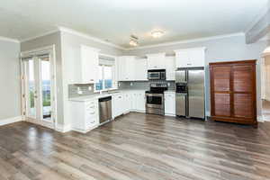 Basement kitchen with stainless steel appliances, crown molding, white cabinets, and backsplash