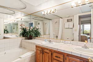 Bathroom with a relaxing tiled bath, dual bowl vanity, and mirror