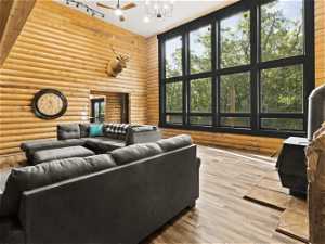 Living room featuring log walls, a high ceiling, ceiling fan, and light hardwood floors