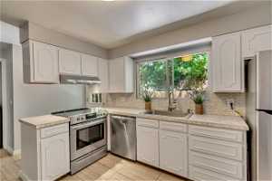 Kitchen with backsplash, light countertops, white cabinetry, stainless steel appliances, and light tile flooring