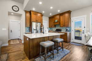 Kitchen with a center island, range, brown cabinets, light countertops, light hardwood flooring, backsplash, and stainless steel fridge with ice dispenser