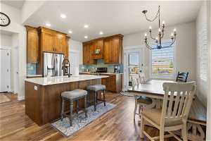 Kitchen featuring a notable chandelier, a center island, stainless steel refrigerator with ice dispenser, range, brown cabinets, light countertops, backsplash, and light hardwood floors