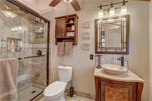 Bathroom with toilet, walk in shower, ceiling fan, tile floors, and large vanity