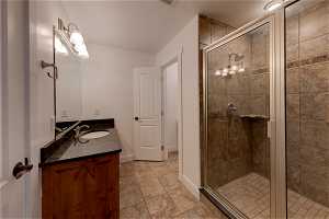 Bathroom featuring vanity with extensive cabinet space, mirror, a shower with door, and light tile floors