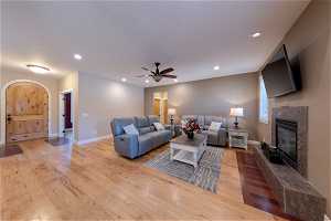 Living room with a fireplace, light hardwood floors, and ceiling fan