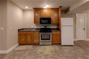 Kitchen featuring light tile flooring, white refrigerator, dark countertops, brown cabinets, and stainless steel range