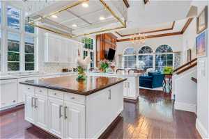 Kitchen with a notable chandelier, plenty of natural light, an island with sink, white cabinets, hardwood flooring, white dishwasher, ornamental molding, and backsplash