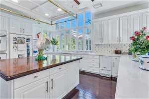 Kitchen featuring coffered ceiling, white cabinets, white oven, dark hardwood flooring, light stone countertops, backsplash, and built in fridge