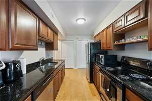 Kitchen featuring appliances with stainless steel finishes, brown cabinets, light hardwood floors, and dark granite counters