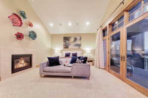 Primary main floor suite with a fireplace, vaulted ceiling, light carpet, and french doors to deck