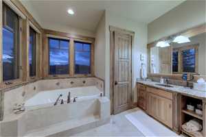 2nd main floor master bathroom with vanity with extensive cabinet space, tiled bath, mirror, and light tile floors
