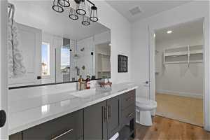 Bathroom with light hardwood flooring, large vanity, a shower with shower door, and mirror
