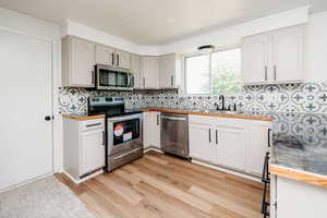 Kitchen featuring white cabinets, backsplash, light hardwood floors, and appliances with stainless steel finishes