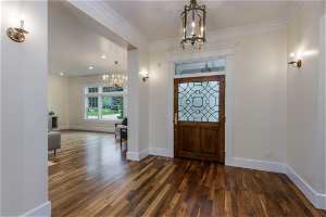 Entrance foyer with crown molding, dark hardwood flooring, and a notable chandelier
