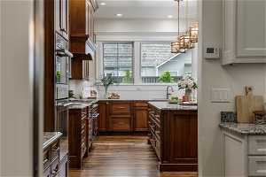 Kitchen with range with gas cooktop, refrigerator, light stone counters, dark hardwood flooring, and dark brown cabinets