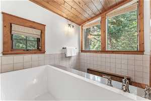 Bathroom with a washtub, vaulted ceiling, a healthy amount of sunlight, wooden ceiling, and tile walls