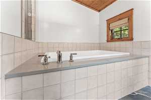 Bathroom with wood ceiling, tile walls, and tiled bath
