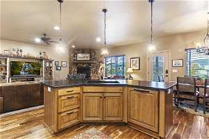 Kitchen featuring hanging light fixtures, brown cabinets, light hardwood floors, ceiling fan, a fireplace, and dark countertops