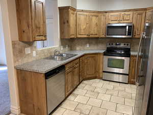 Kitchen featuring appliances with stainless steel finishes, backsplash, light tile flooring, and brown cabinets