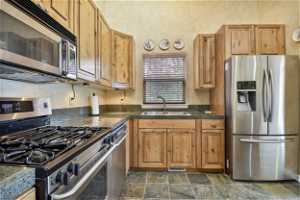 Kitchen featuring stainless steel appliances, dark countertops, brown cabinets, and dark tile flooring