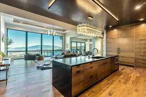 Kitchen featuring a chandelier, dark countertops, light hardwood flooring, kitchen island with sink, and dishwashing machine