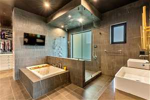 Bathroom featuring tile walls, mirror, double sink vanity, separate shower and tub, and light tile flooring