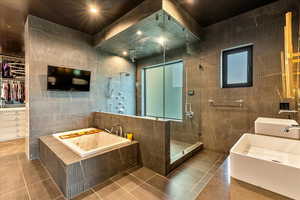 Bathroom featuring tile walls, mirror, double sink vanity, separate shower and tub, and light tile flooring