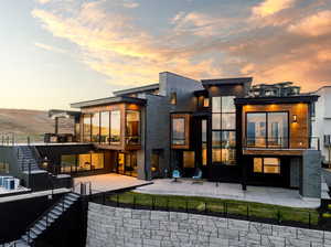 Back house at dusk featuring a balcony and a patio