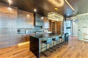 Kitchen with custom range hood, a center island, dark countertops, range, brown cabinets, backsplash, and light hardwood floors