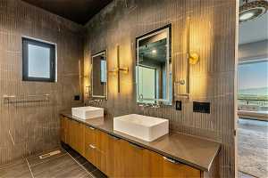 Bathroom with dual large vanity, tile flooring, mirror, and tile walls