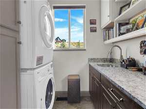 Clothes washing area featuring sink, stacked washer and dryer, cabinets, and dark tile flooring
