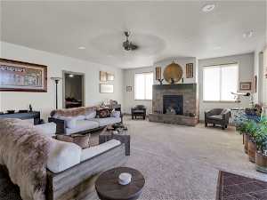 Living room with carpet floors, ceiling fan, and a stone fireplace