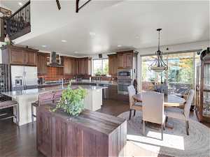 Kitchen featuring stainless steel appliances, a center island, wall chimney exhaust hood, dark hardwood floors, and decorative light fixtures