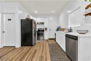 Kitchen featuring light hardwood floors, white cabinets, countertops light, and appliances with stainless steel finishes