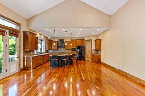 Kitchen with a center island, black fridge with ice dispenser, hanging light fixtures, backsplash, and hardwood flooring