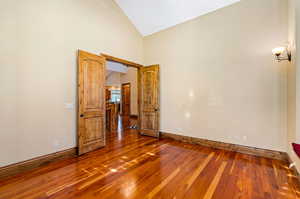 Unfurnished room featuring dark hardwood floors and vaulted ceiling high