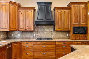 Kitchen with light stone counters, tasteful backsplash, custom range hood, and stainless steel gas cooktop