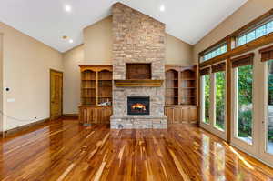 Unfurnished living room featuring a healthy amount of sunlight, hardwood floors, vaulted ceiling high, and a stone fireplace