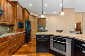 Kitchen featuring backsplash, decorative light fixtures, light hardwood floors, and black appliances