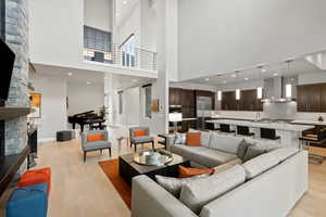 Living room featuring a stone fireplace, a towering ceiling, light wood-type flooring, and sink