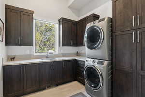 Washroom featuring stacked washer / dryer, sink, light wood-type flooring, and cabinets