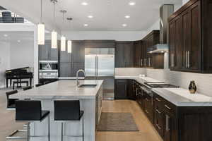 Kitchen with light wood-type flooring, wall chimney exhaust hood, backsplash, pendant lighting, and sink