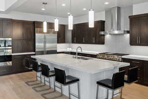 Kitchen with wall chimney range hood, stainless steel appliances, tasteful backsplash, a kitchen island with sink, and sink