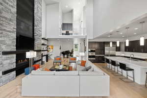 Living room featuring sink, a stone fireplace, a high ceiling, and light hardwood / wood-style flooring