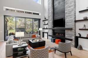 Living room with a high ceiling, a stone fireplace, and wood-type flooring