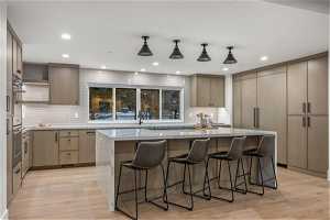 Kitchen featuring backsplash, light hardwood / wood-style flooring, pendant lighting, and a center island