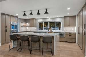 Kitchen featuring hanging light fixtures, appliances with stainless steel finishes, a center island, tasteful backsplash, and light wood-type flooring